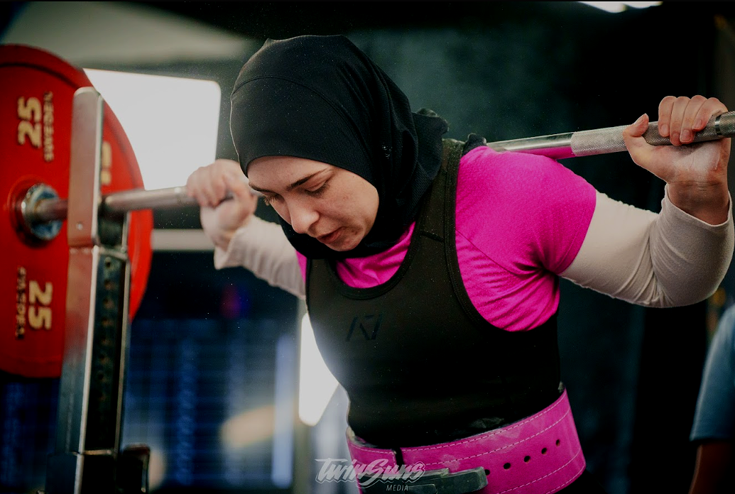 A woman lifting a barbell loaded with red weights at a gym.