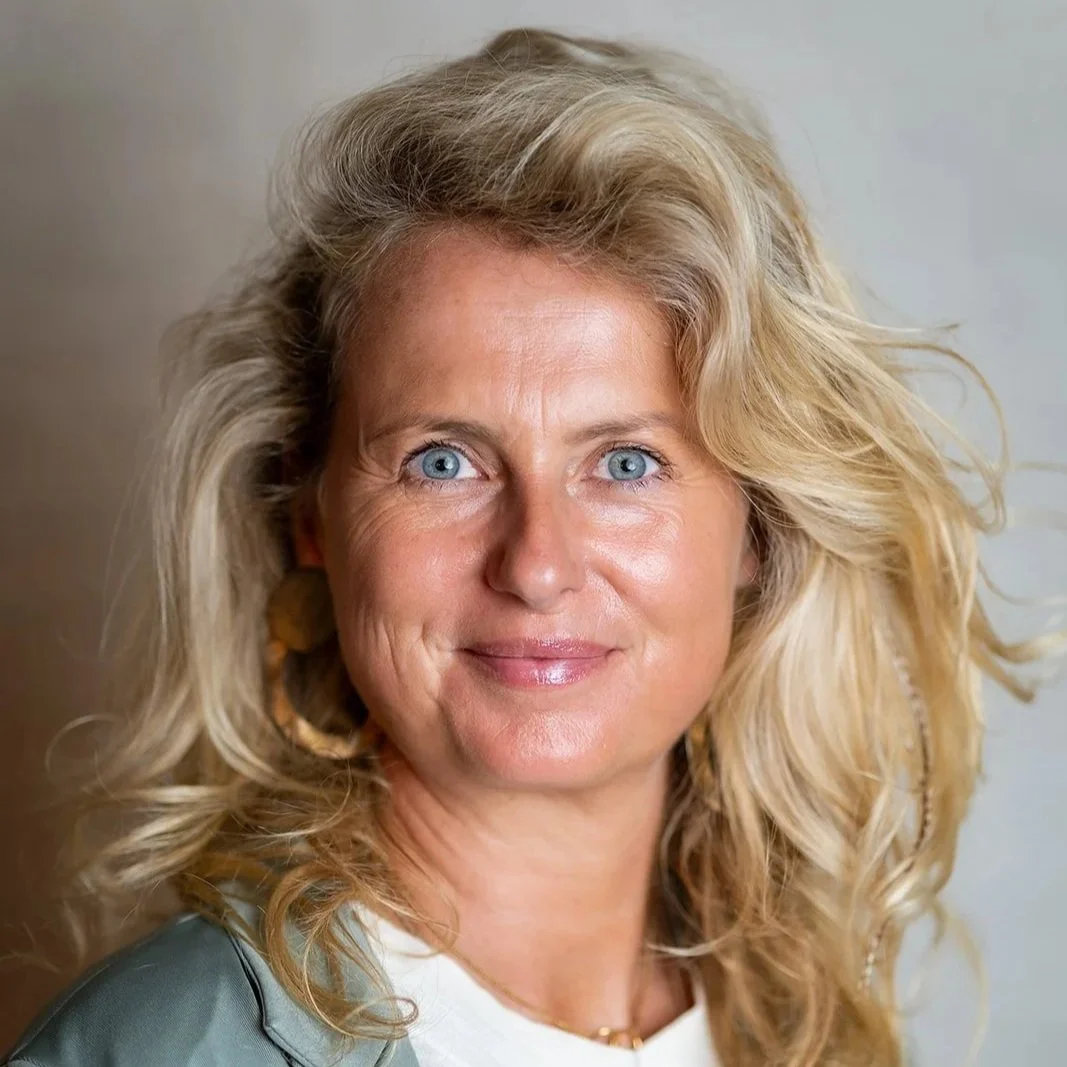 Close-up van een lachende vrouw met golvend blond haar en blauwe ogen.