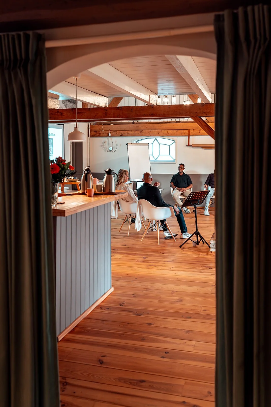 Mensen hebben een vergadering of presentatie in een rustieke kamer met houten plafonds en vloeren, met een flip-over en een scherm.