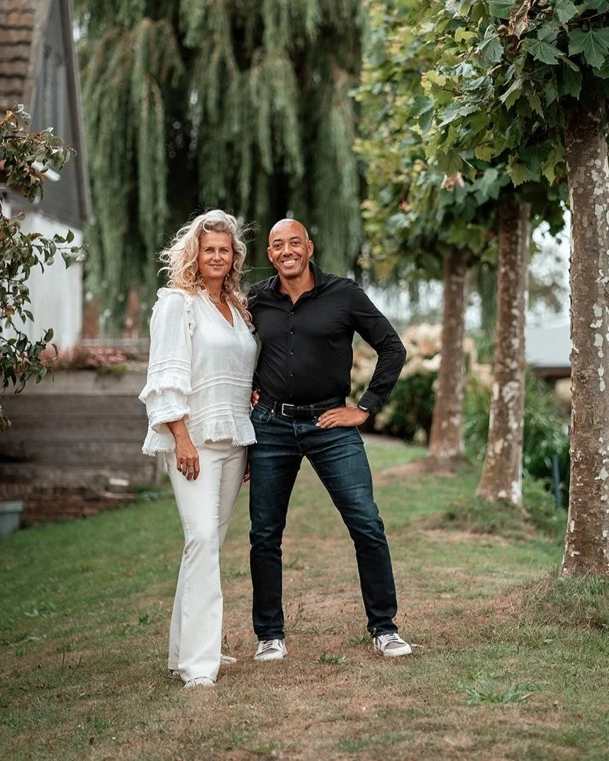 Twee mensen staan samen in een tuin met bomen op de achtergrond.