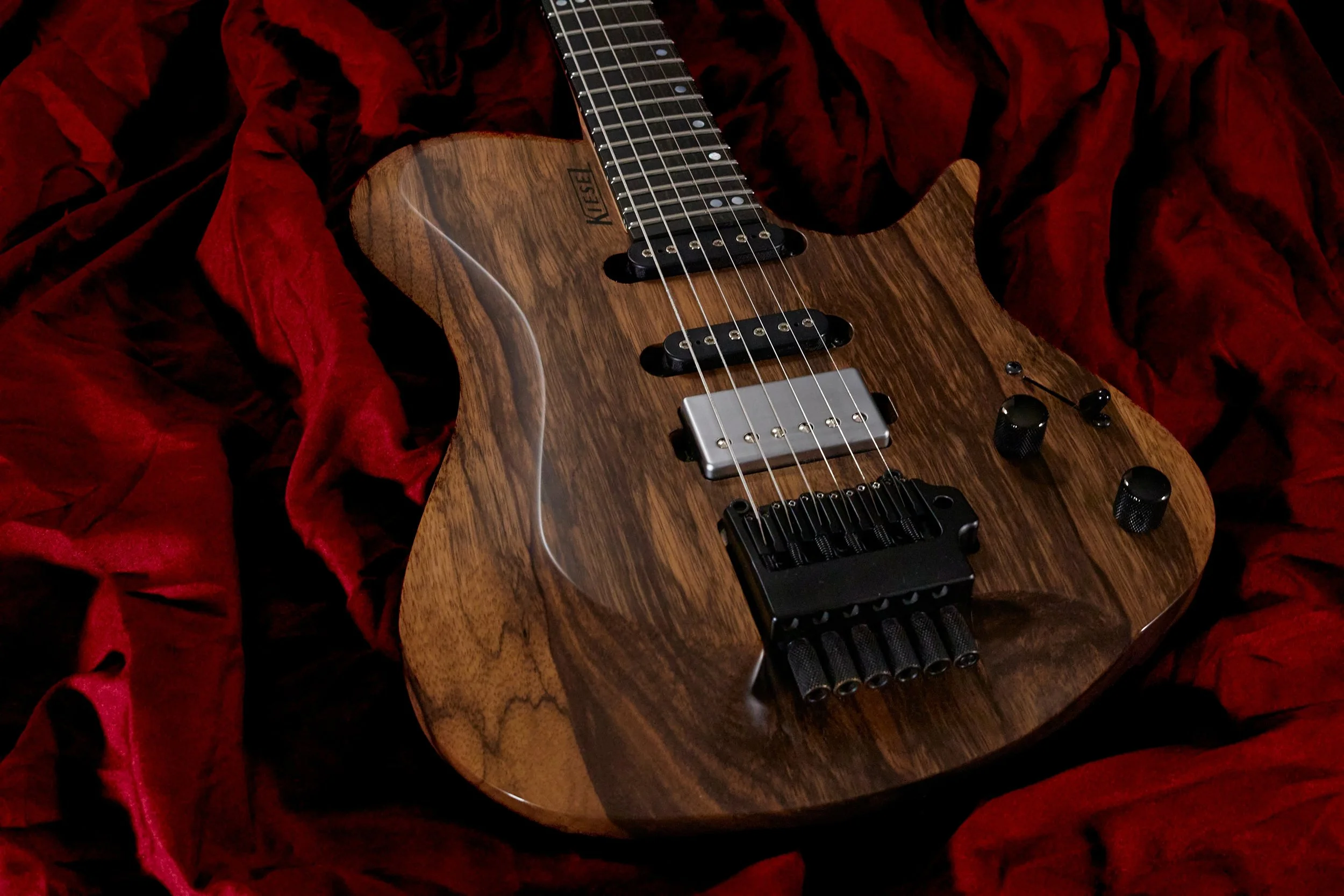 An electric guitar with a wooden finish, black hardware, and a focus on the body, resting on red velvet fabric.