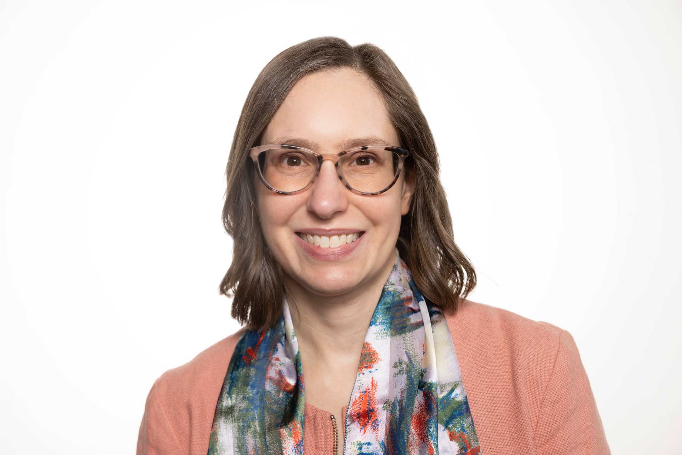 Photo of Emily, a white woman with glasses and shoulder-length brown hair wearing a silk scarf