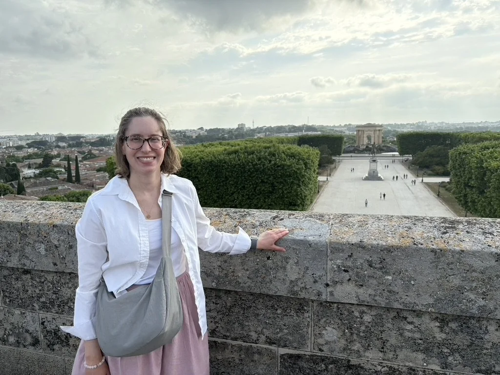 Photo of Emily on top of the Arc de Triomphe in Montpellier with the historic water tower of Peyrou and a Louis XIV statue in the background