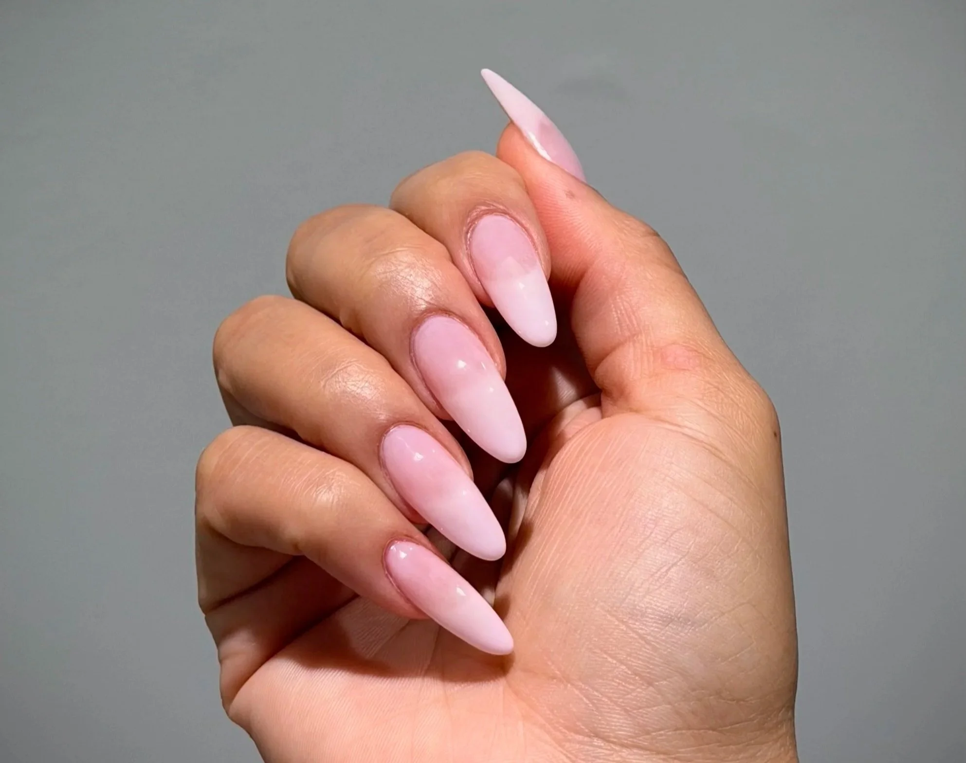 Close-up of a hand with long, almond, light pink gel-x nails.