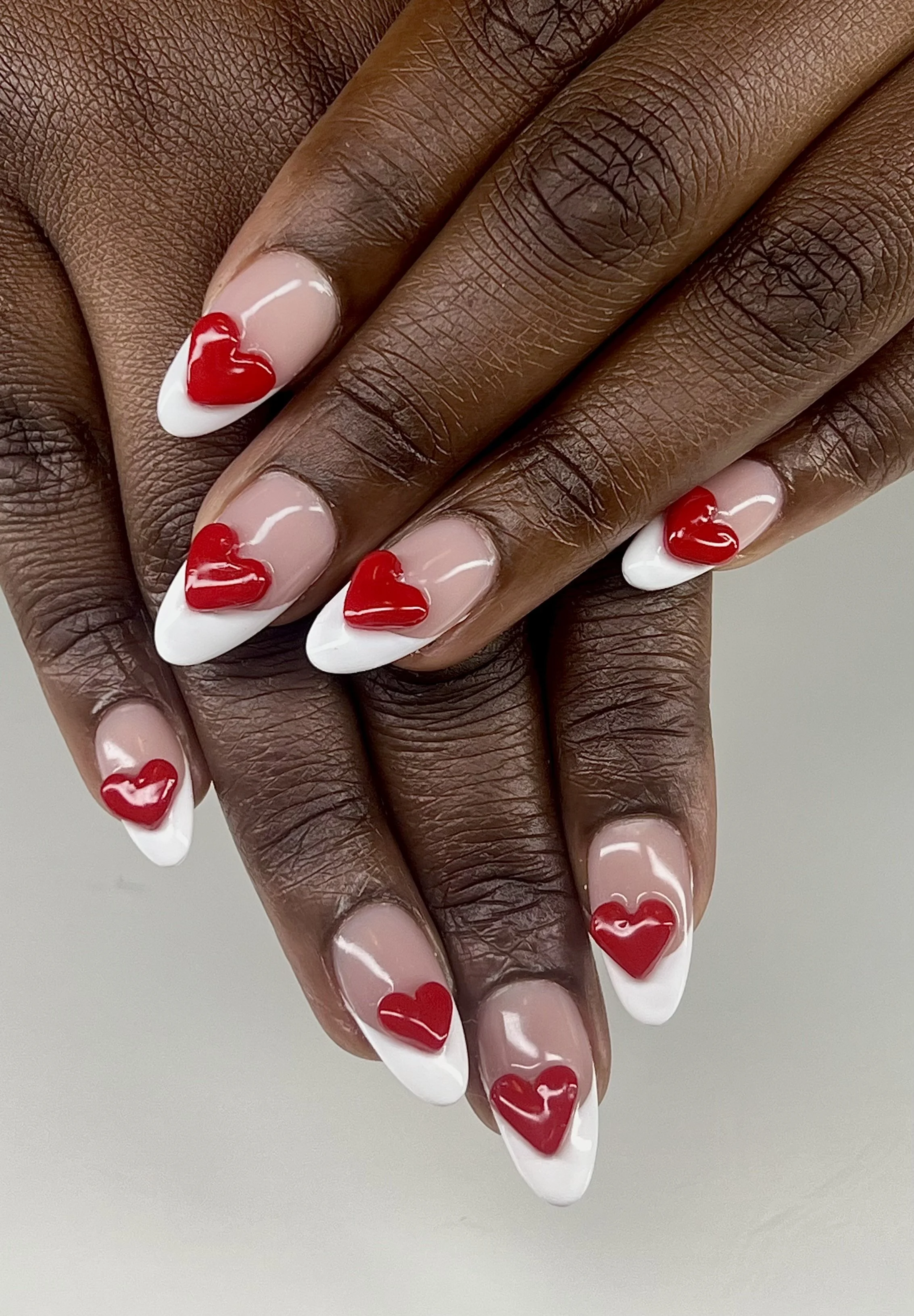 Close-up of dark-skinned hand with French manicure nails decorated with red heart-shaped designs.