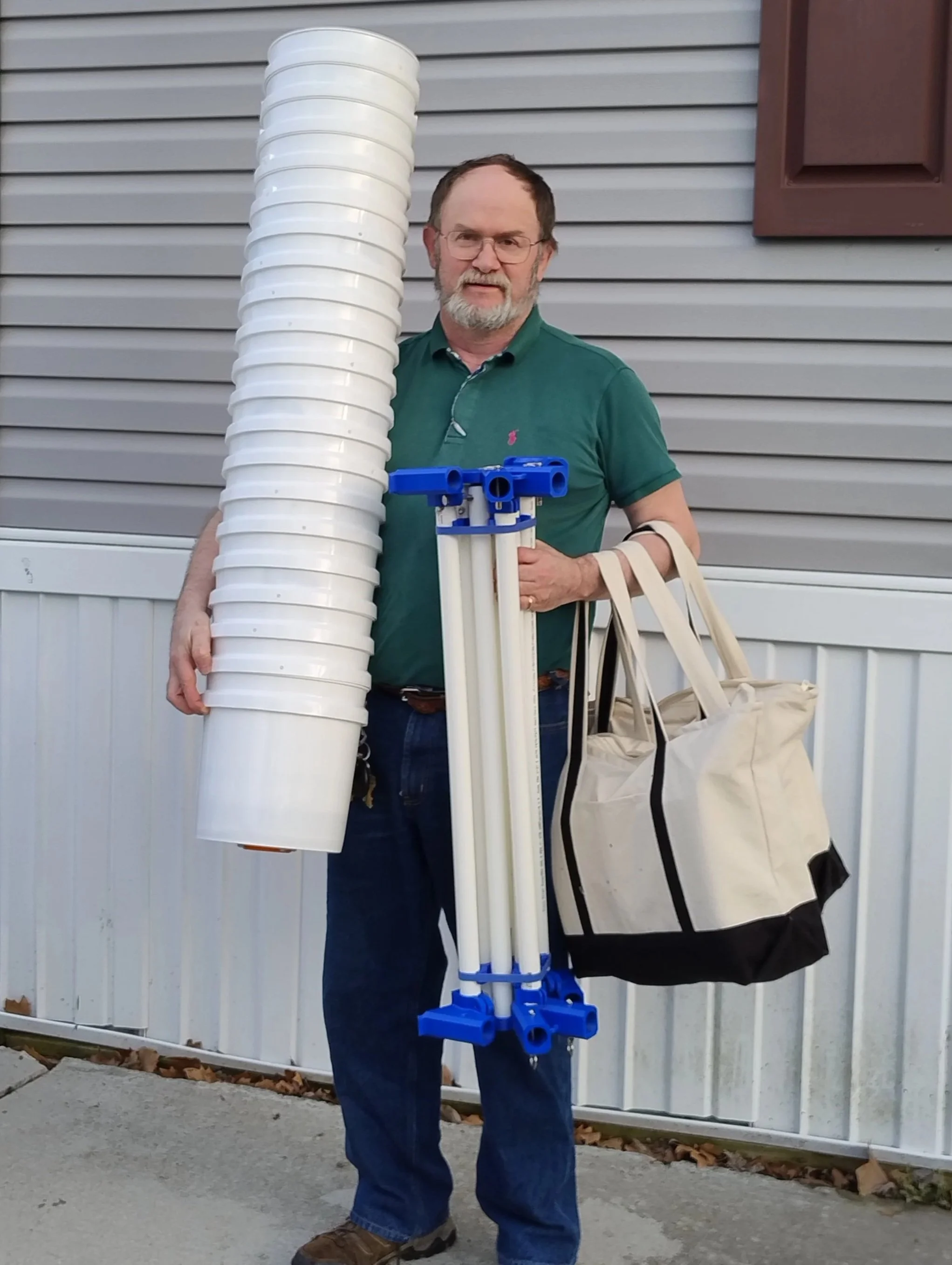 A man with glasses, a beard, and a green polo shirt holding a Marino Customs Drone Testing Lane Kit in front of a house with beige siding.