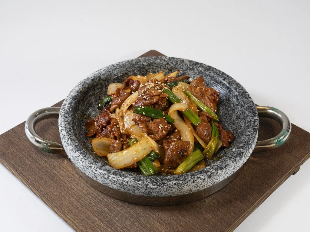 Stir-fried beef with onions, green onions, and sesame seeds served in a stone bowl.