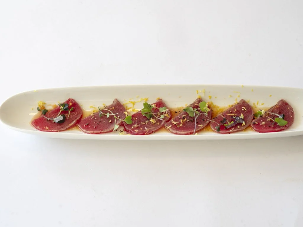 Sliced raw tuna steak garnished with microgreens and lemon zest on a long white plate