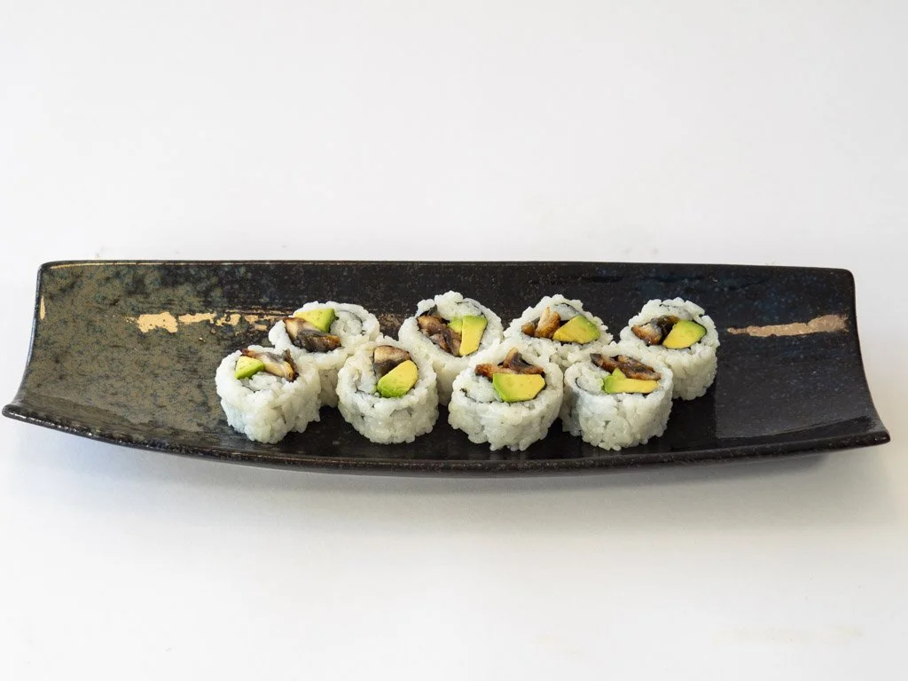 Sushi rolls with avocado and possibly mushroom or eel on a black rectangular plate