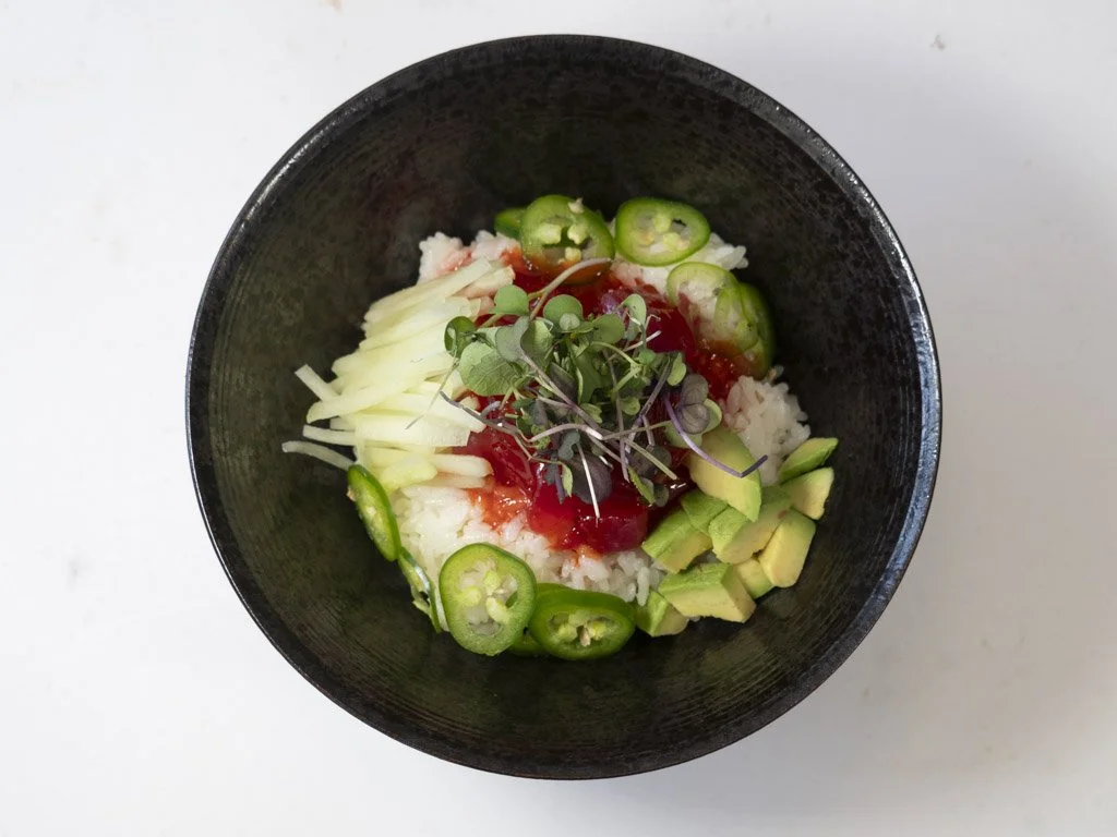 Bowl of rice topped with sliced jalapeños, avocado, shredded cheese, microgreens, and salsa.