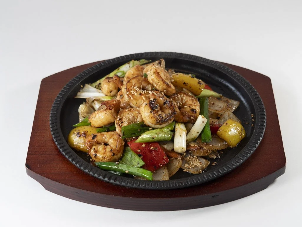 Shrimp stir-fry with vegetables served on a sizzling hot plate with sesame seeds