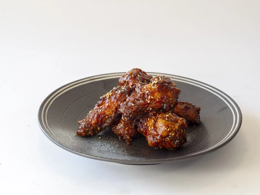Plate of spicy glazed chicken wings garnished with sesame seeds on a black plate.