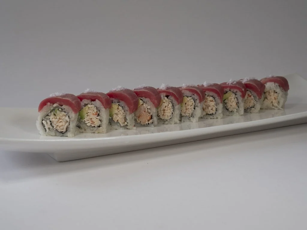 A long white platter with ten pieces of sushi roll topped with slices of raw fish, served on a plain light gray background.