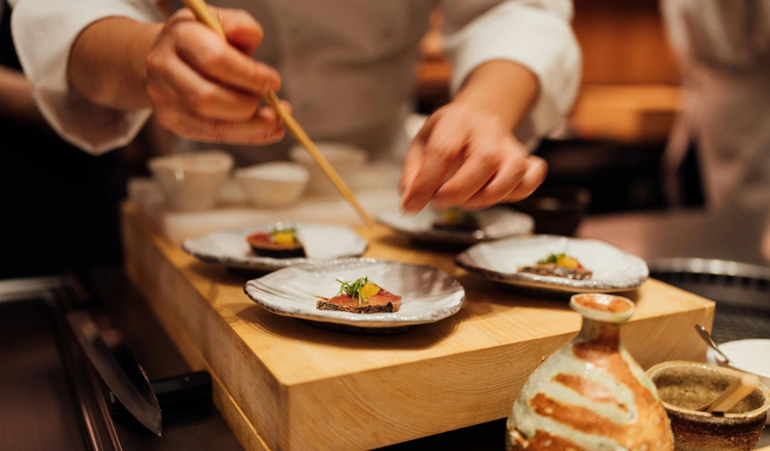 Chef plating small, elegant dishes in a restaurant kitchen.