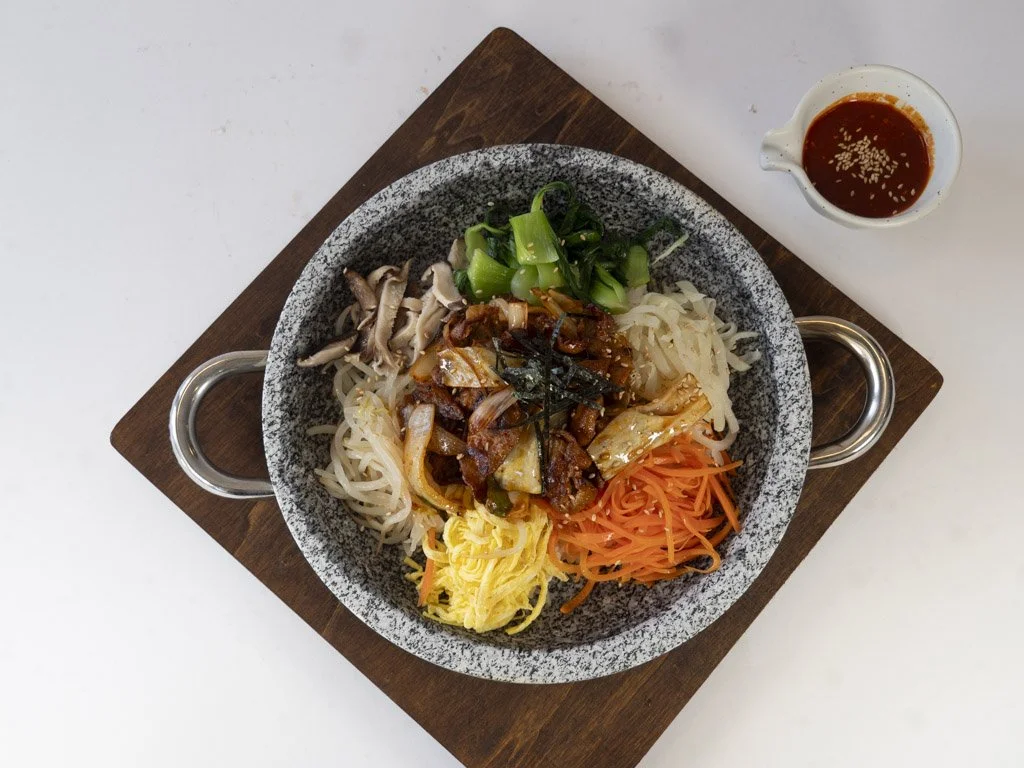Assorted vegetable bibimbap in a bowl with a side of sauce on a wooden tray.