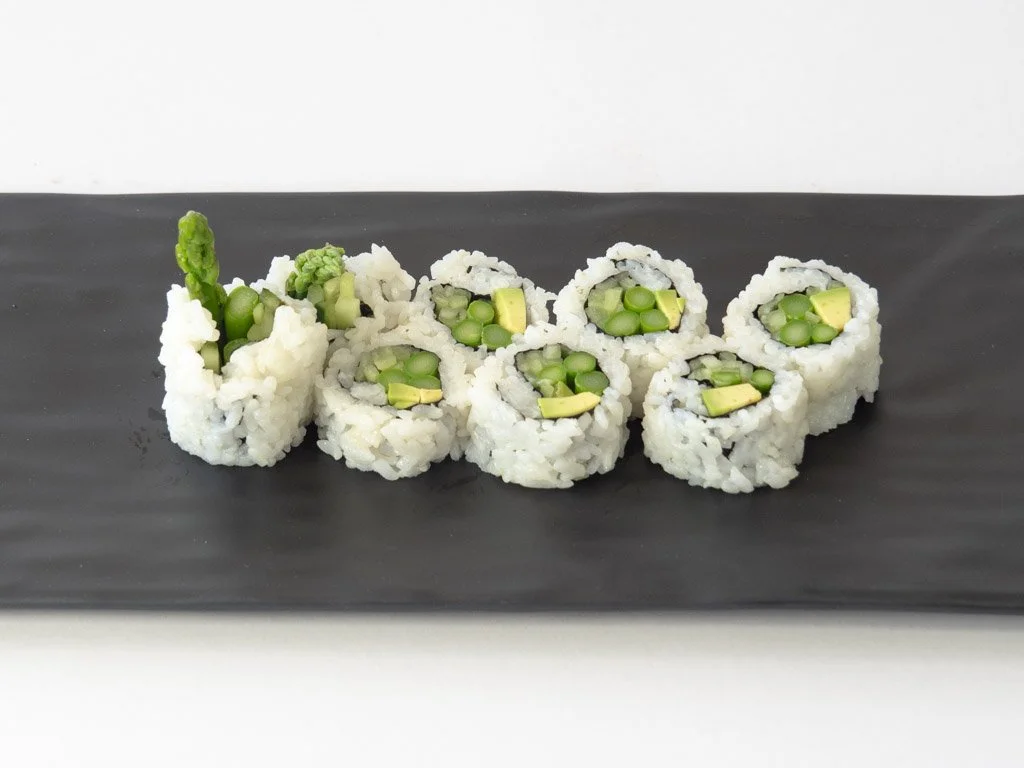 Close-up of six pieces of cucumber sushi roll with rice, served on a black rectangular plate