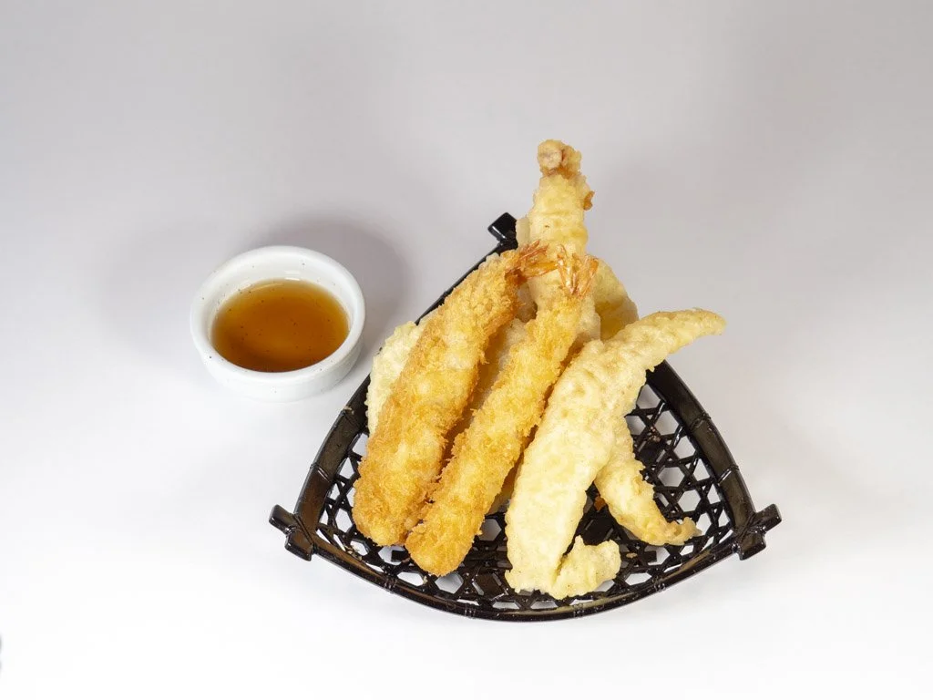 Fried fish fillets and tempura vegetables served with a bowl of dipping sauce on a white background.