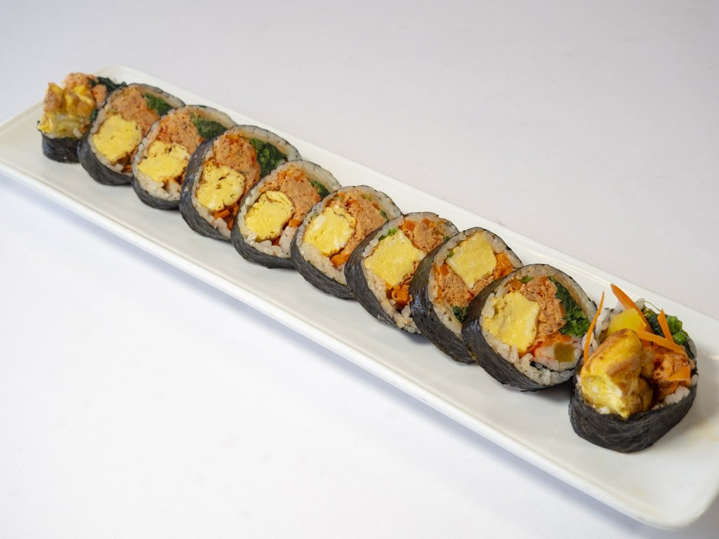 Sushi rolls on a white platter with various fillings, including egg, fish roe, and vegetables, garnished with thin carrot and vegetable slices.