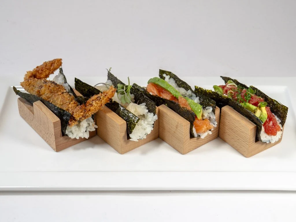 Four pieces of sushi with seaweed, rice, and various toppings on a white rectangular plate.