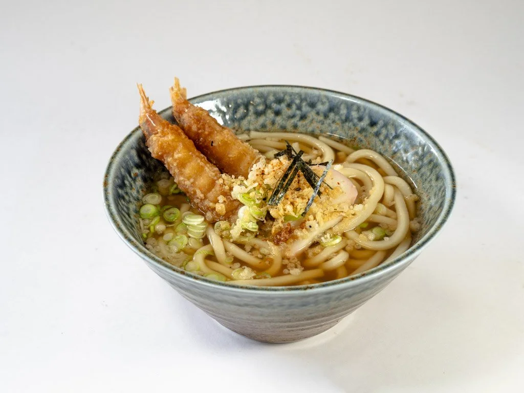 Bowl of Japanese ramen with two tempura shrimp, noodles, green onions, and seaweed garnish.
