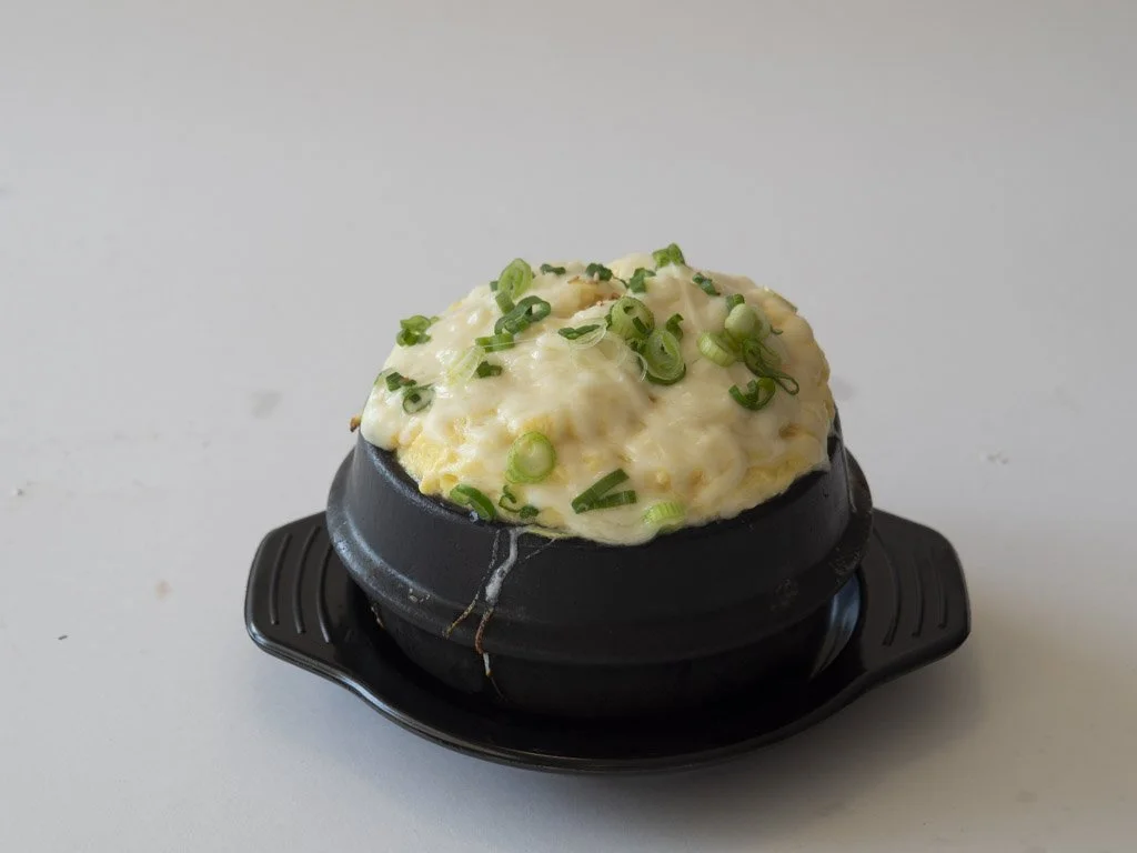 Potato topping with chopped green onions served in a small hot stone bowl on a black tray.
