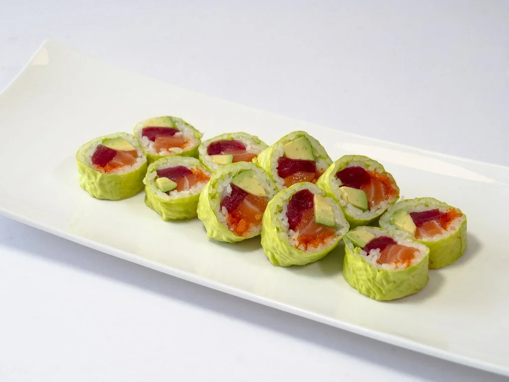 A plate of eight sushi rolls with rice, avocado, salmon, and tuna, wrapped in cucumber slices instead of seaweed.