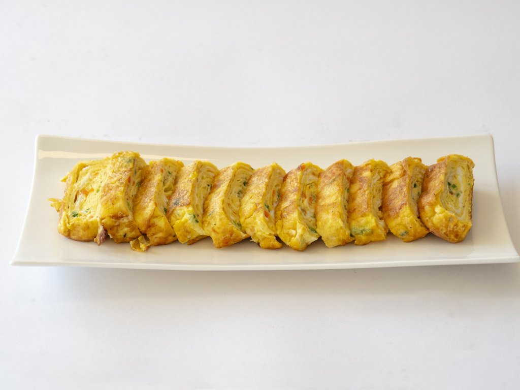 Slices of a rolled omelette with visible vegetables on a rectangular white plate