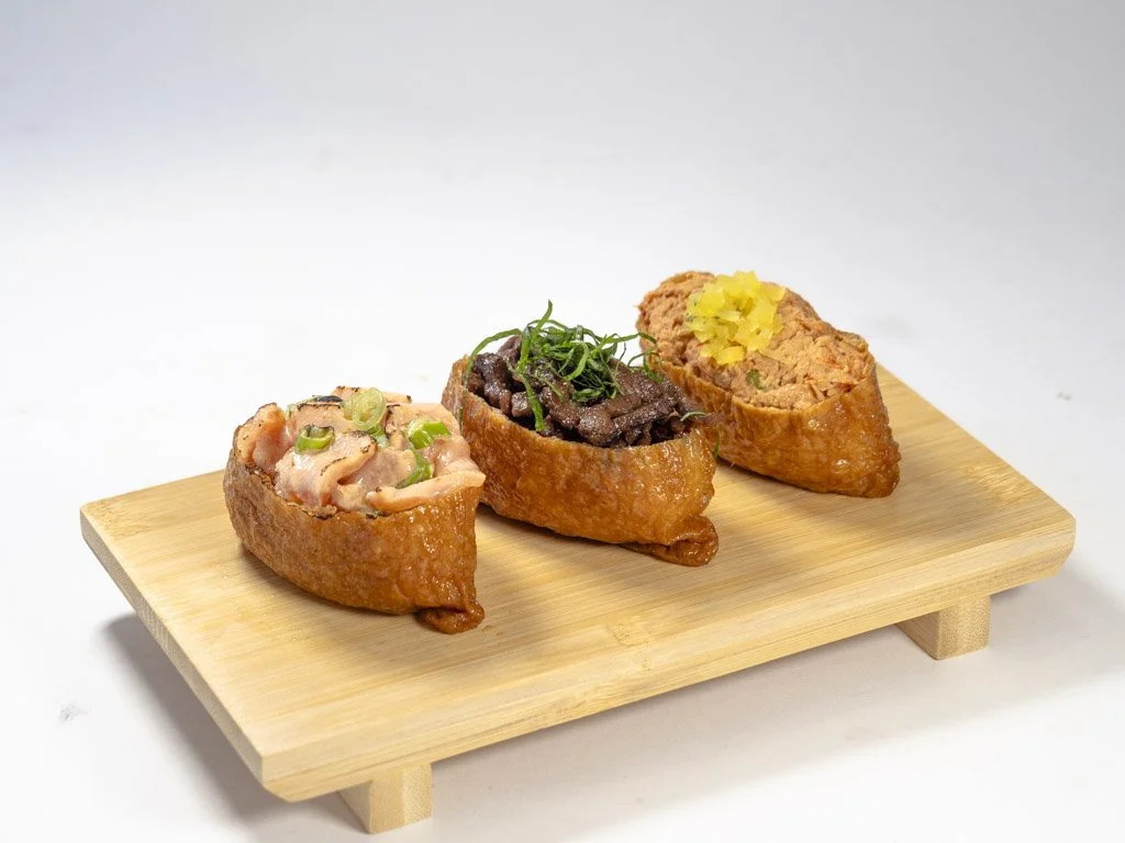 Three inari sushi pieces on a small wooden tray with white background.