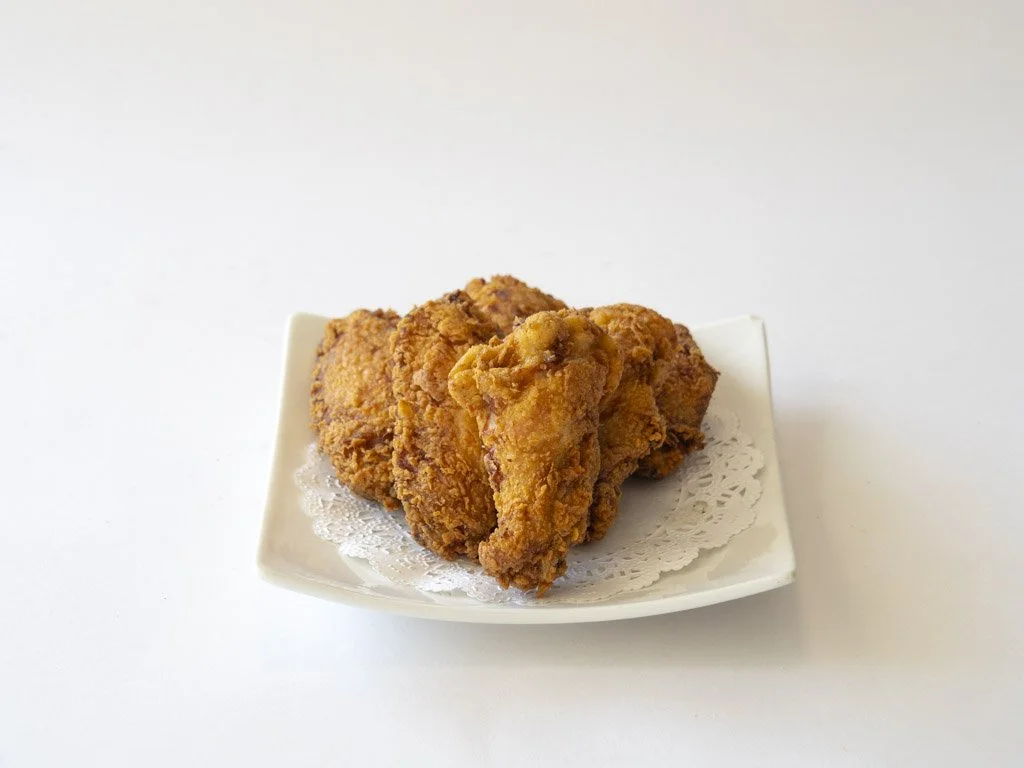 Fried chicken drumsticks and pieces on a white plate with a paper doily