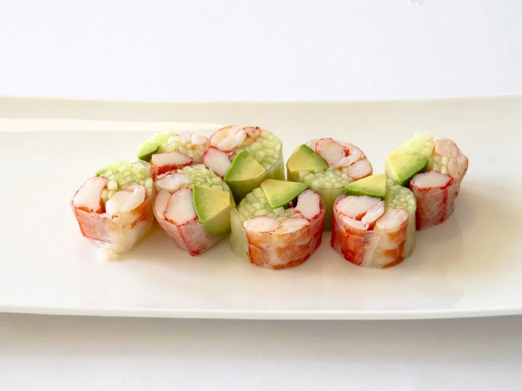Sushi rolls filled with shrimp, cucumber, and avocado on a white rectangular plate.