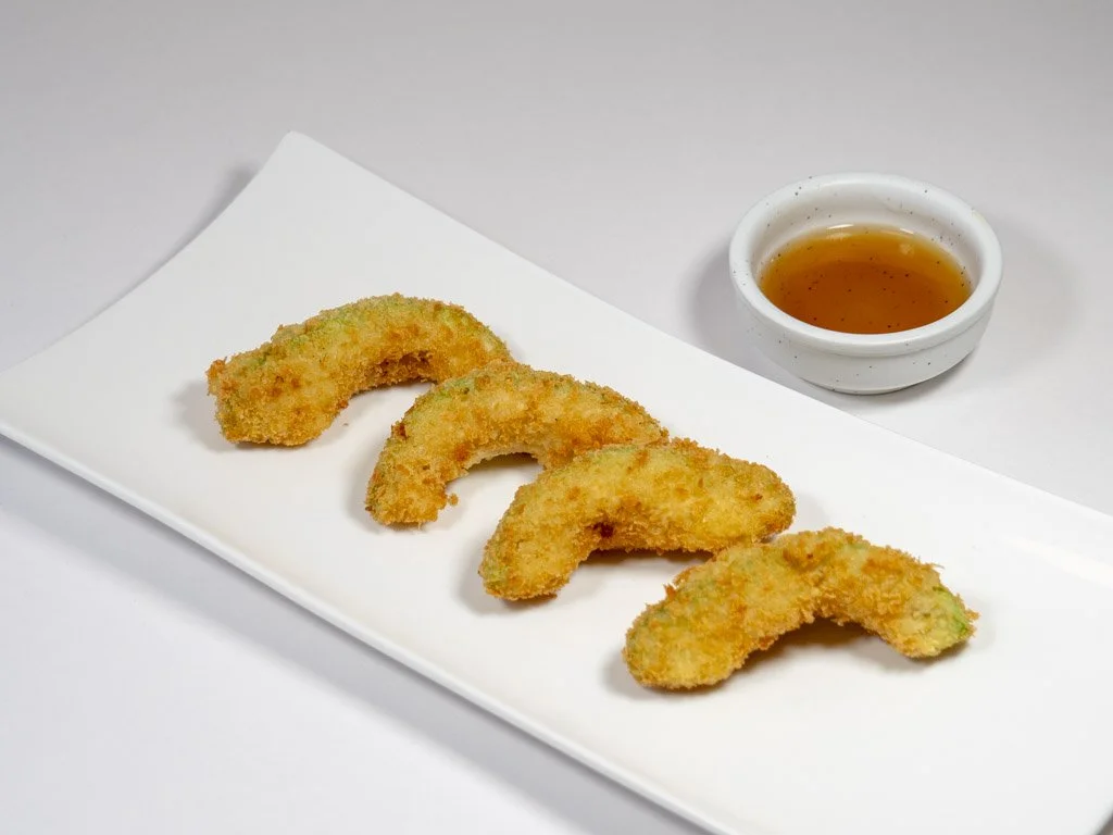 Four pieces of breaded and fried calamari rings on a white rectangular plate, served with a small bowl of dipping sauce.