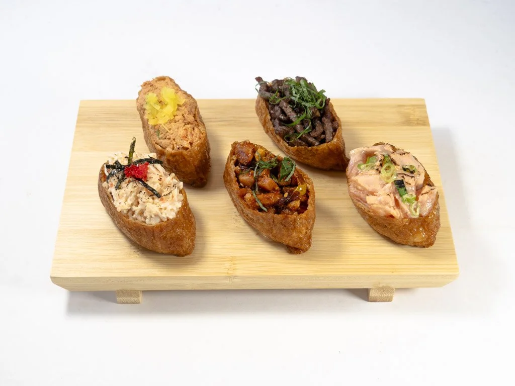 Five different types of Japanese inarizushi with various fillings, served on a wooden tray.