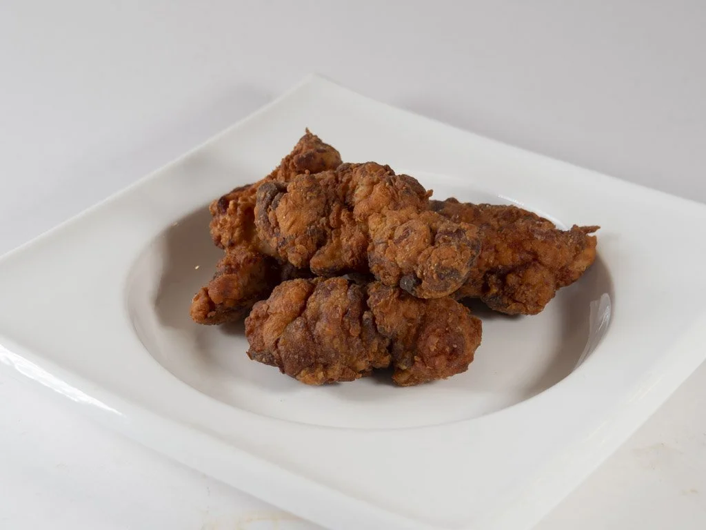 Three pieces of fried chicken on a white square plate with a small indent.