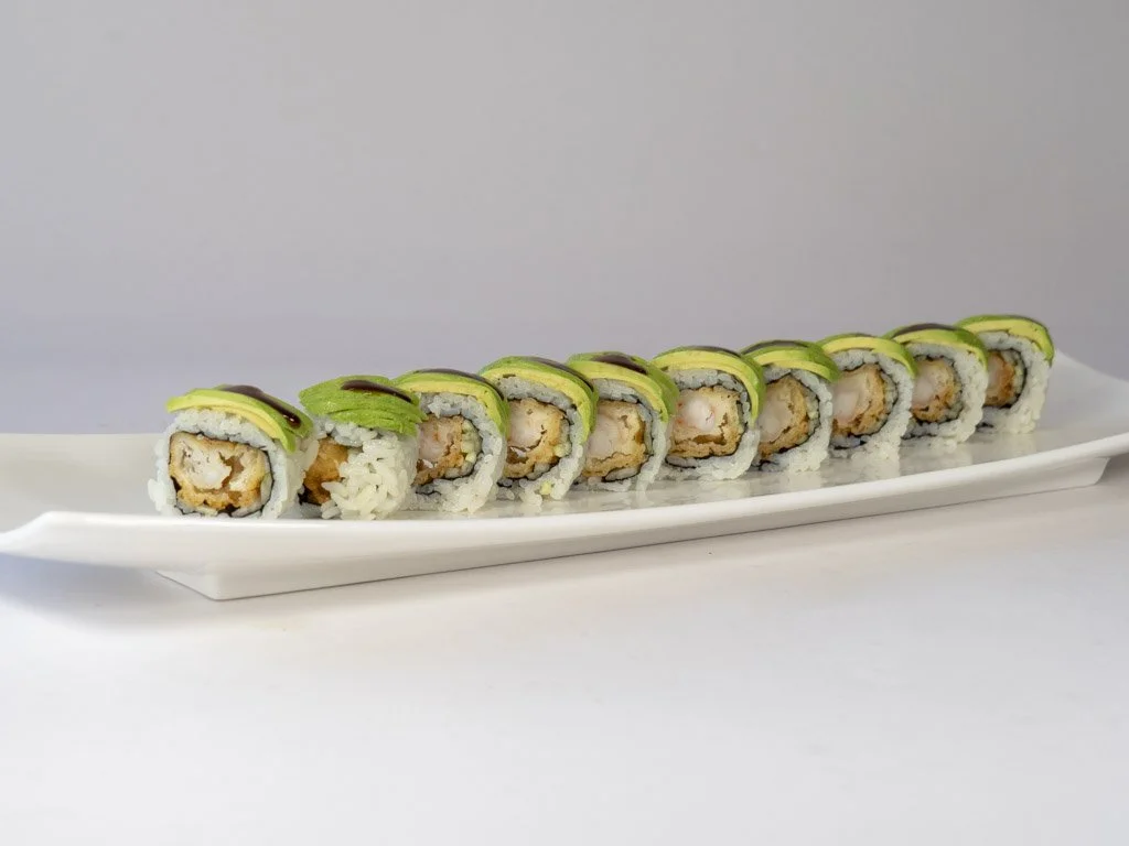 Plate of sushi rolls with avocado and cooked seafood, sliced showing interior ingredients, on a white rectangular platter with a plain background.