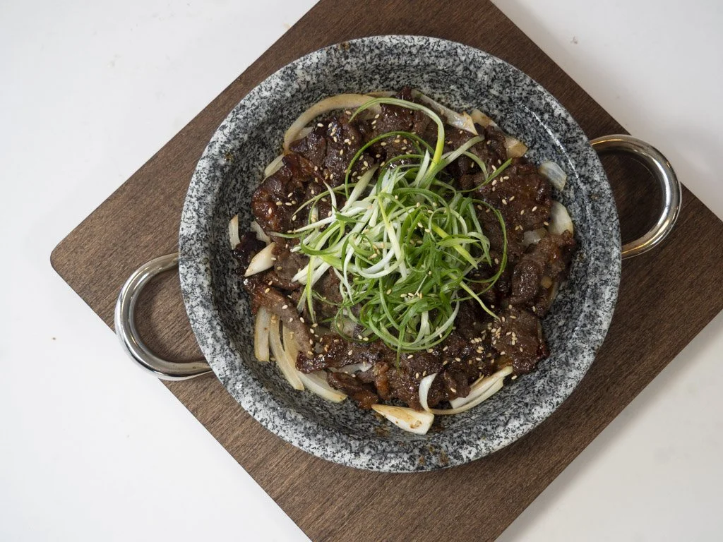 Bowl of Asian-style beef noodle stir-fry topped with green sprouts and sesame seeds, served on a wooden board