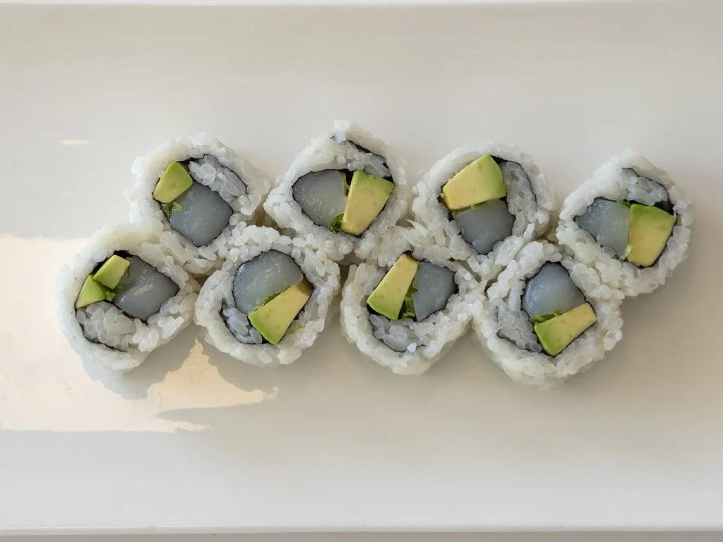 Sushi rolls with avocado and fish on a white plate.