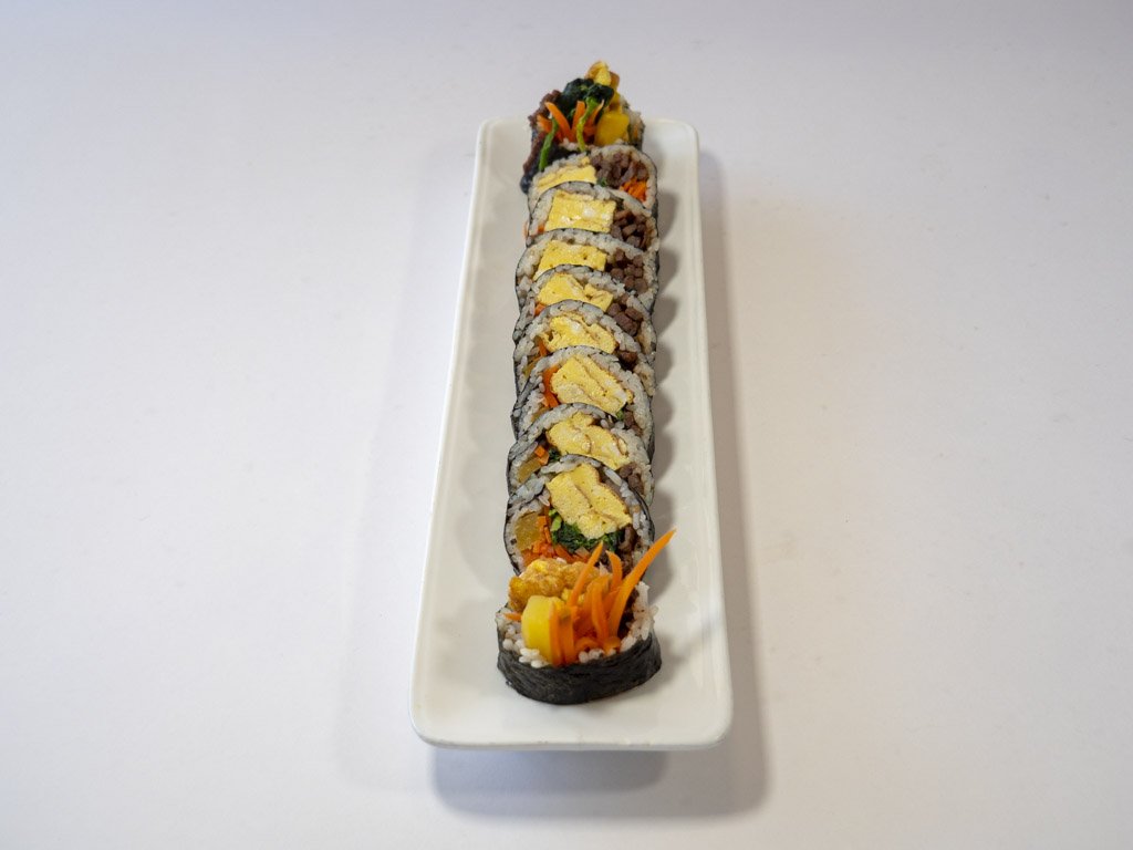 A plate of sushi rolls garnished with shredded carrots and yellow pickled radish on a white rectangular dish.
