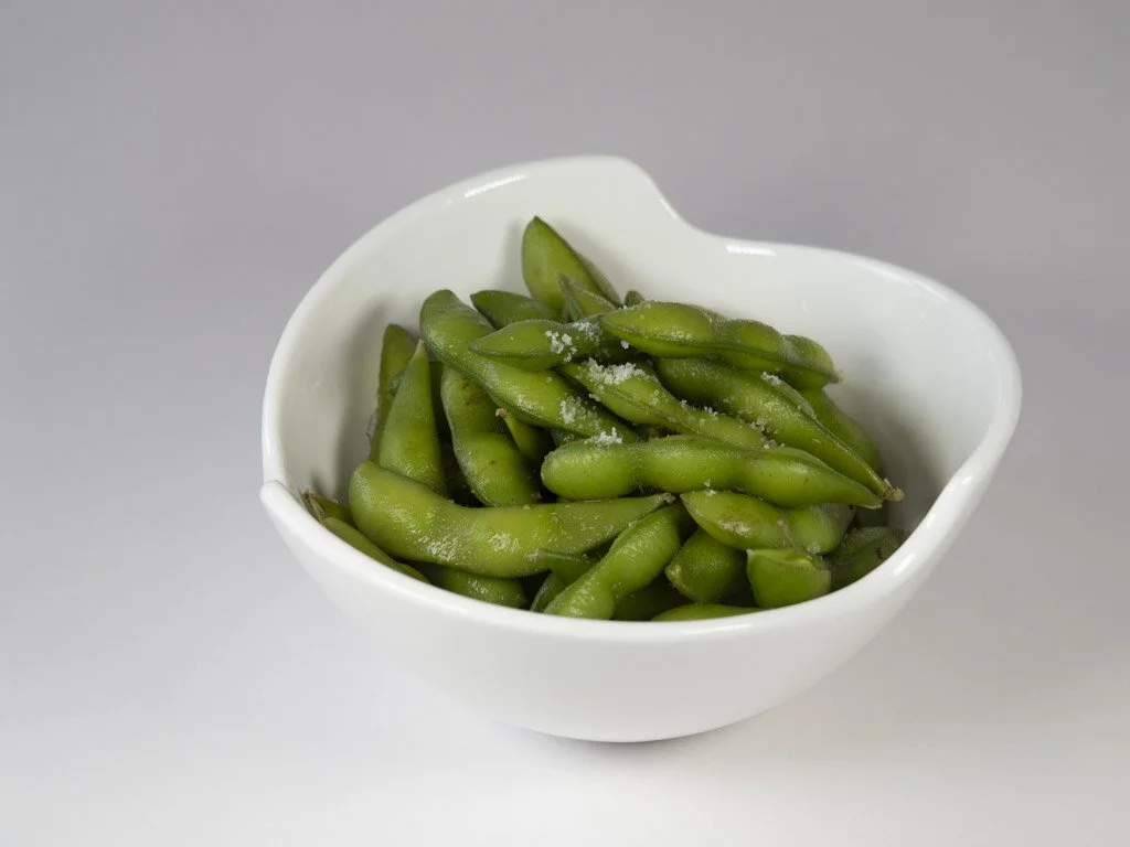 White bowl filled with salted edamame beans on a light gray background.