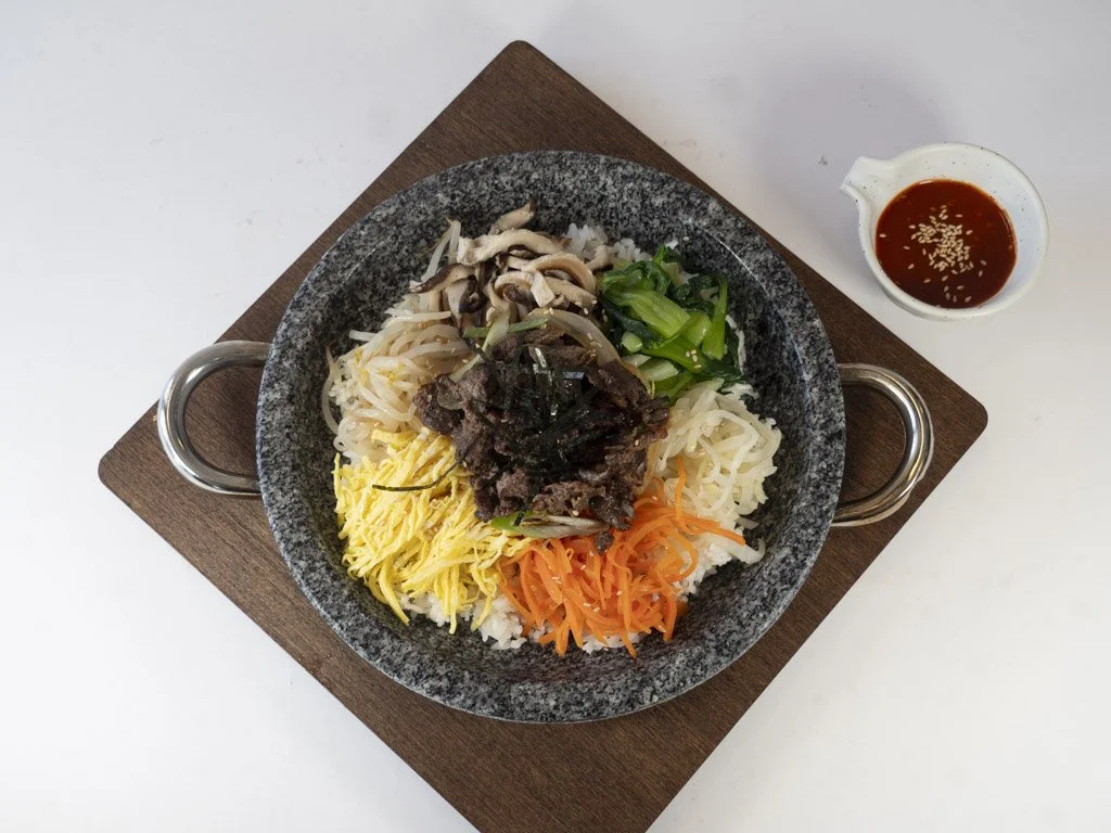 Korean bibimbap served with assorted vegetables, beef, and a side of spicy sauce.