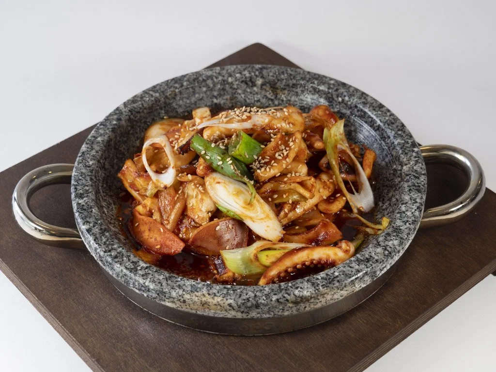 Korean spicy stir-fried octopus with vegetables and sesame seeds served in a stone bowl