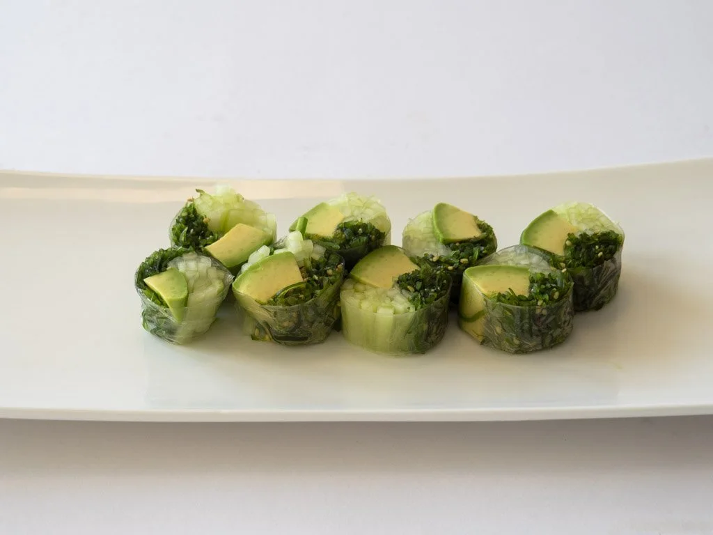 Fresh cucumber and avocado rolls with chopped herbs on a white rectangular plate