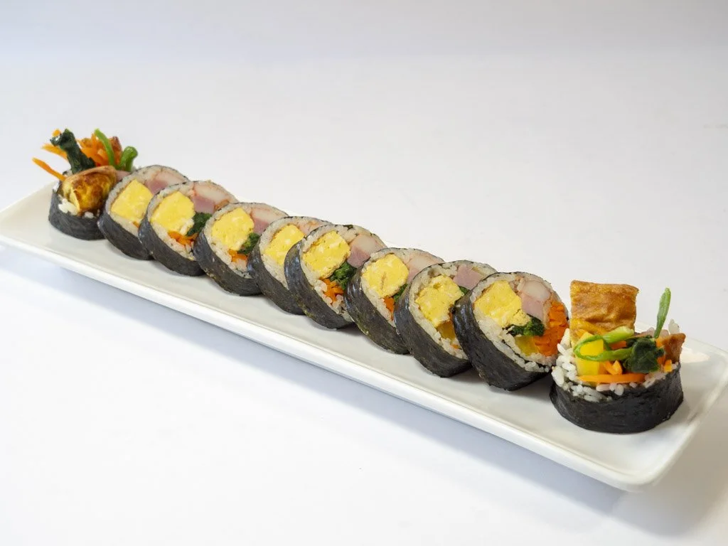Sushi rolls with seaweed wrapping, filled with egg, vegetables, and fish, arranged on a white rectangular plate.