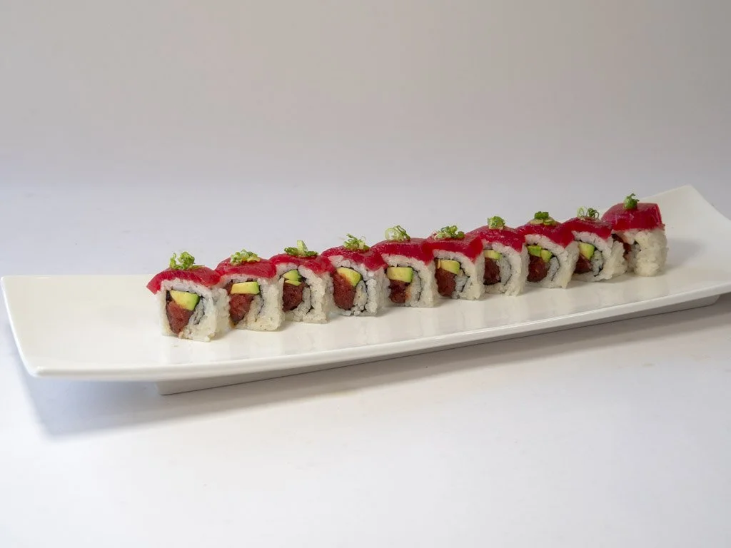 Sushi rolls with tuna, avocado, and cucumber garnished with green onions on a white rectangular plate