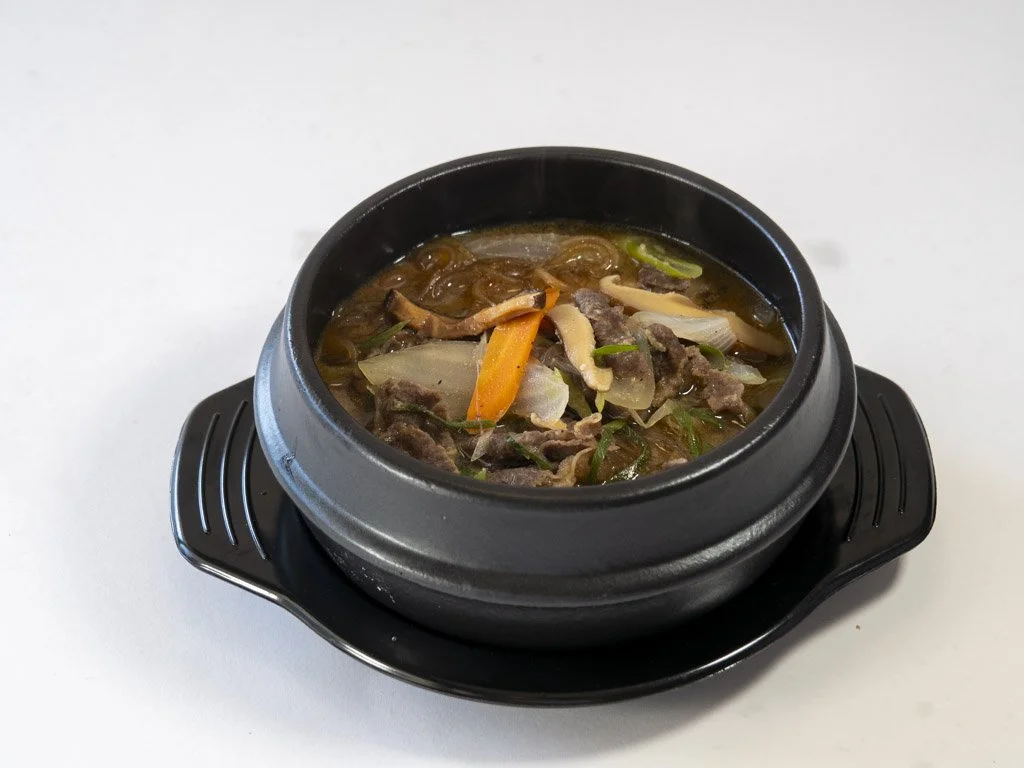 Hot stone bowl filled with beef and vegetable soup, including carrots, onions, and green onions.