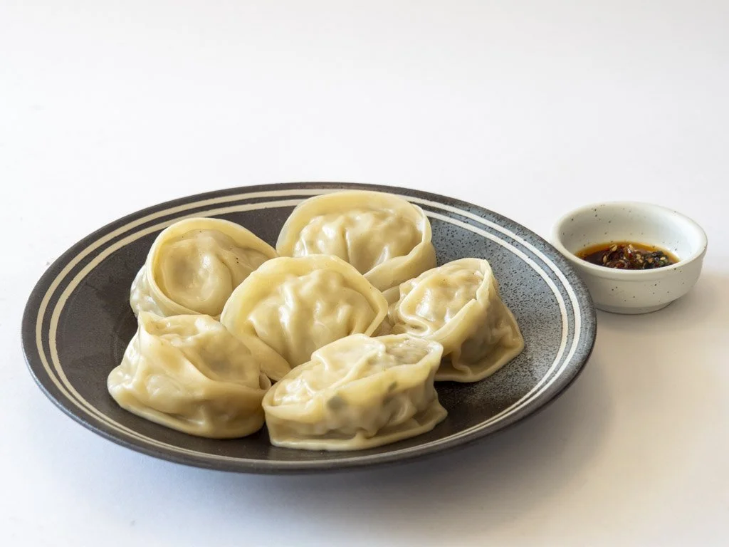 Plate of steamed dumplings with a small bowl of soy sauce on the side.