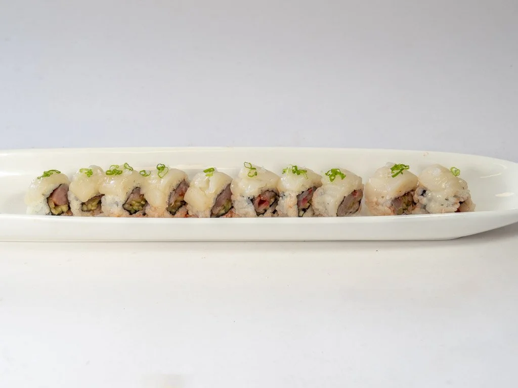 A long white platter with several pieces of sushi topped with white sauce and green onion sprinkled on top.