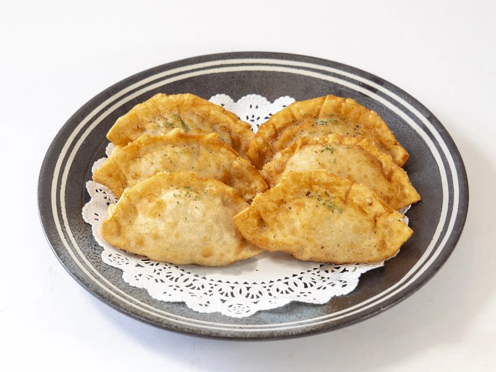 Six cooked pierogis on a black plate with white rim and doily lining.