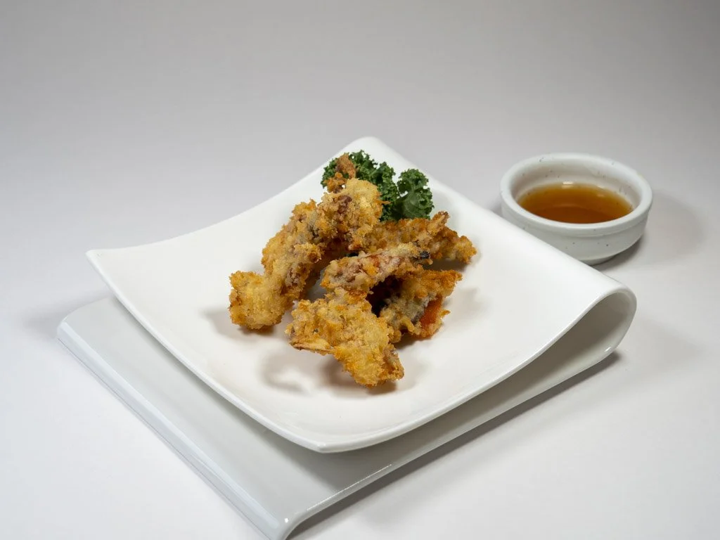 Fried calamari with dipping sauce and a sprig of parsley on a white plate.