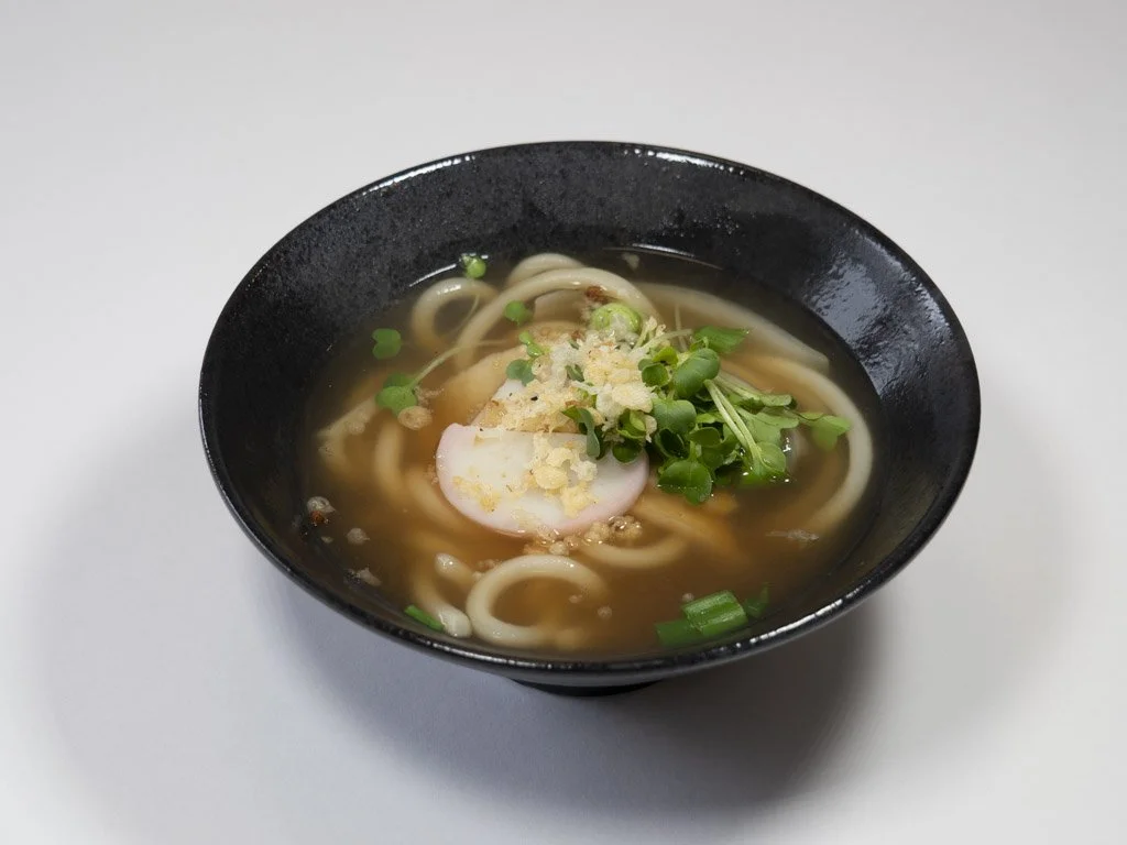 A bowl of hot noodle soup with green garnishes, a poached egg, and chopped green onions.