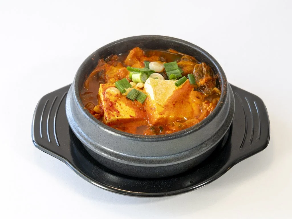 Hot Korean stew with tofu, green onions, and vegetables in a black stone pot